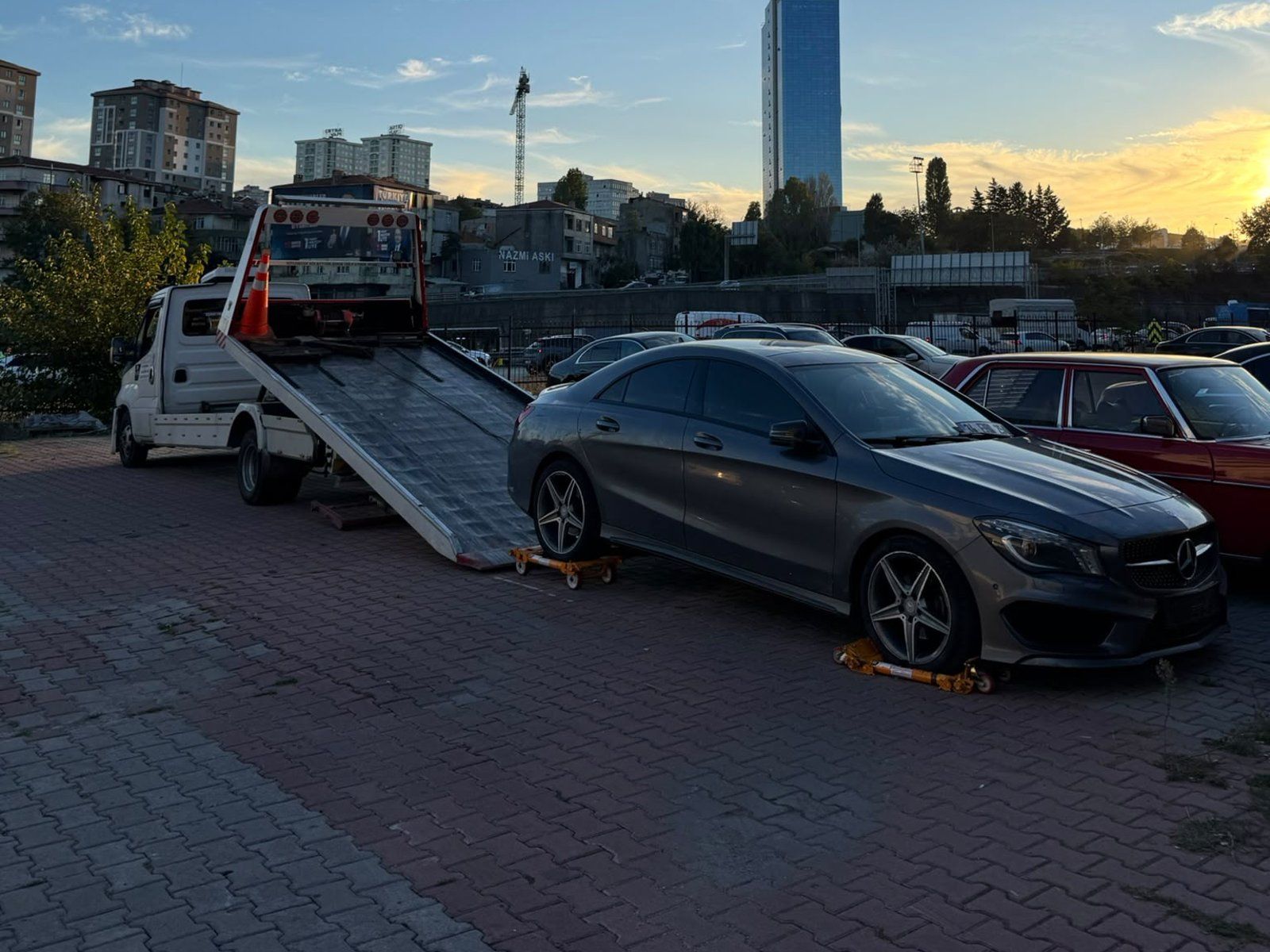 Tekerlekleri altında sarı taşıma aparatları olan otomobil, rampası indirilmiş çekicinin önünde
