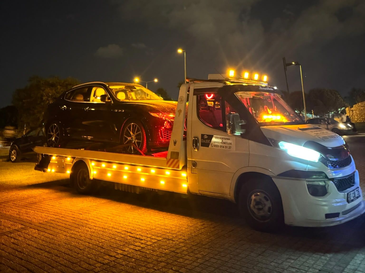 Gece tepe lambaları yanan Dask Oto Kurtarma çekicisi, kasasında siyah otomobil